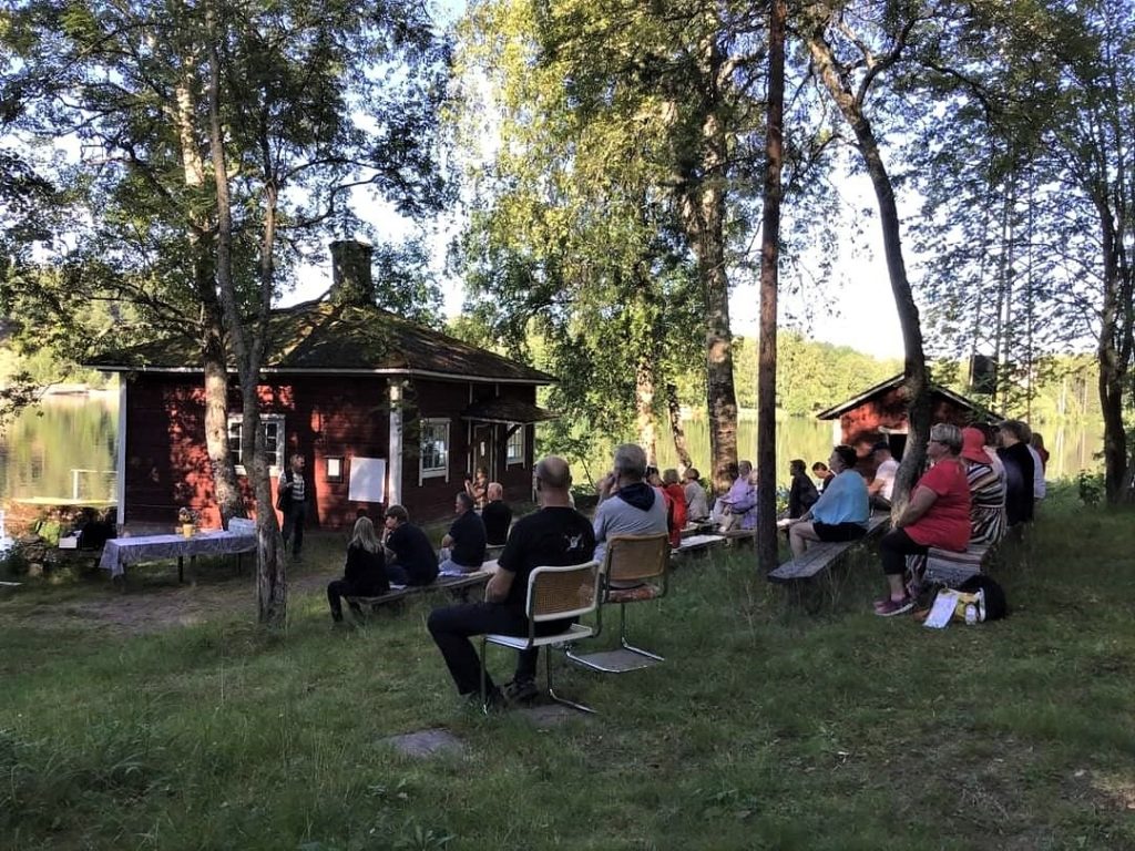 Ihmisiä asukastapahtumassa kuuntelemassa puhetta Jyrängön historiasta rantatuvalla.