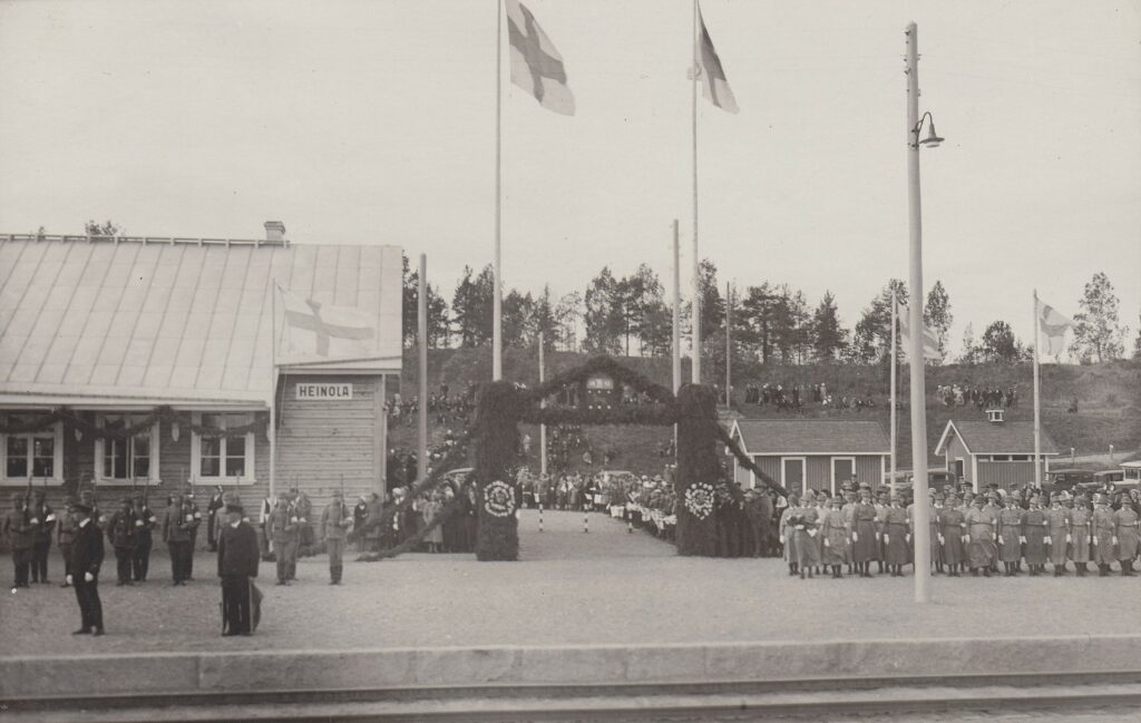 Heinola rautatieasema juhlaliputuksessa, vasemmalla suojeluskuntalaiset ja oikealla lotat odottamassa presidentin junaa.