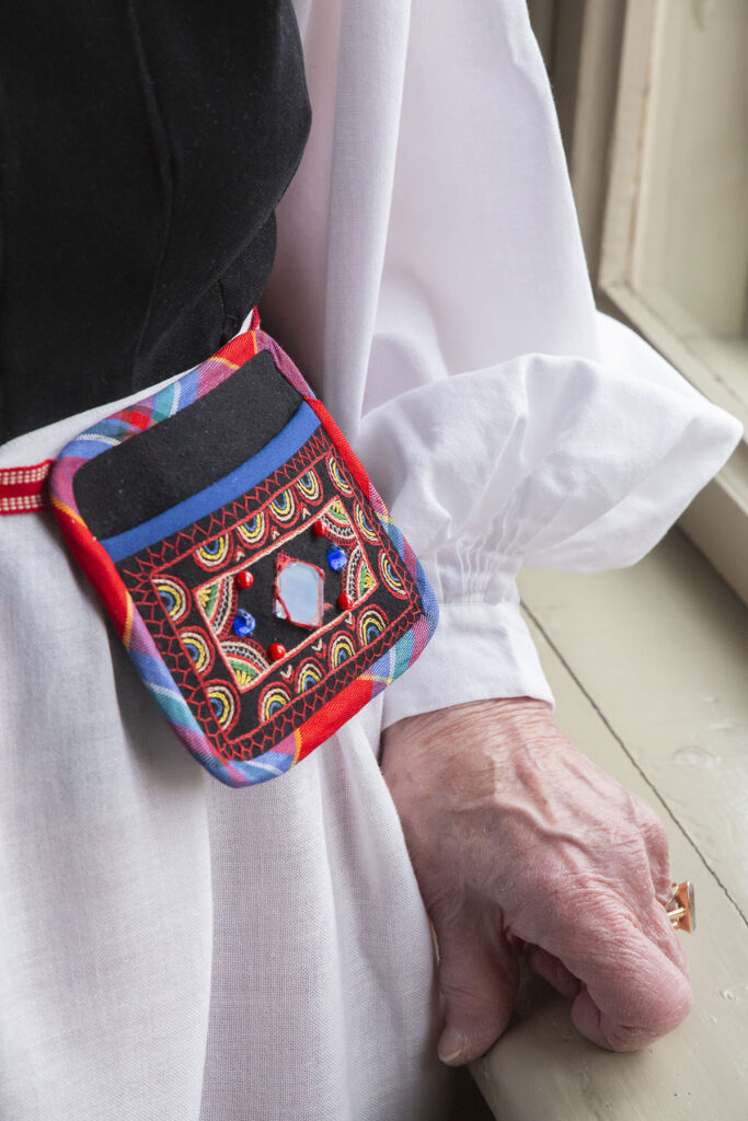 Kuva Leena Alhon Iitin puvusta ja siihen kuuluvasta kirjailusta pienestä laukusta, joka puetaan vyötärölle.